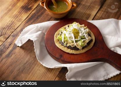 Sopes de Pollo. Traditional homemade Mexican appetizer prepared with fried corn dough covered with refried beans, green or red sauce, lettuce, cheese, onion and shredded chicken