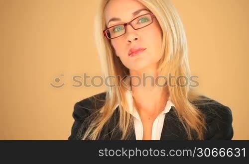 Sophisticated blonde businesswoman wearing glasses smiling at the camera on a brown studio background