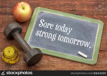 Sore today, strong tomorrow fitness concept - slate blackboard sign against weathered red painted barn wood with a dumbbell, apple and tape measure