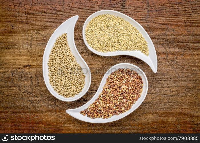 sorghum, millet and buckwheat - three gluten free grains in teardrop shaped bowls against rustic wood