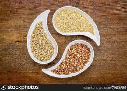 sorghum, millet and buckwheat - three gluten free grains in teardrop shaped bowls against rustic wood