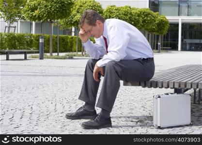 Sorrowful businessman sitting on a bench in front of an office building