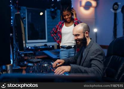 Sound engineer and female singer at remote control panel in audio recording studio. Musician in headphones listens composition, professional music mixing. Sound engineer and female singer, recording studio