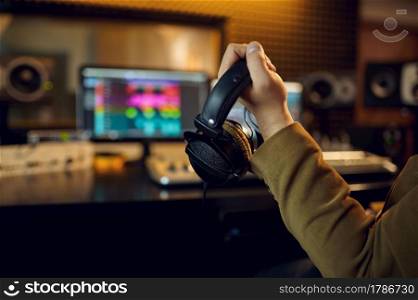 Sound engineer hand holds headphones holds microphone, recording studio interior on background. Synthesizer and audio mixer, musician workplace. Engineer hand holds headphones, recording studio