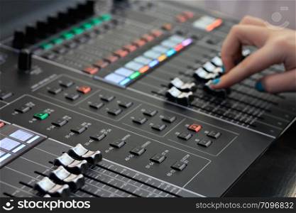 Sound mixing board with hand on faders in the background. Close up view. Selective focus.