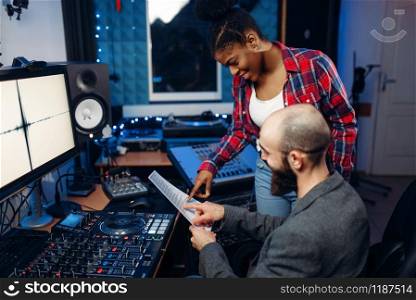 Sound operator and female singer at remote control panel in audio recording studio. Musician at the mixer, professional music mixing. Sound operator and female singer, recording studio