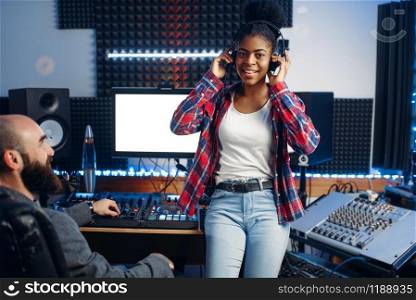 Sound producer and female performer in headphones listens composition in recording studio. Professional audio and music mixing technology. Sound producer and female performer in studio