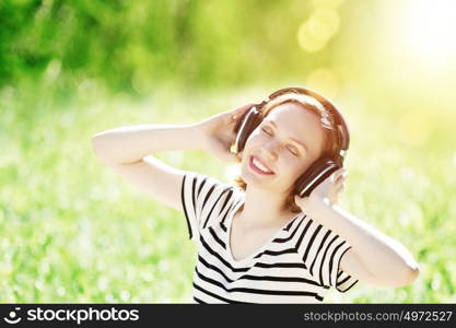 Sounds of nature. Young pretty woman enjoying music in headphones in summer park