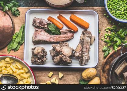 Soup cooking preparation with cooked meat, vegetables, potatoes and green peas on rustic kitchen table, top view