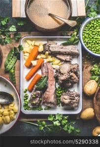 Soup cooking preparation with pot of broth, cooked meat, vegetables, potatoes and green peas on rustic kitchen table, top view