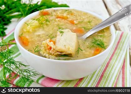 Soup fish kulesh with millet, potatoes and carrots and spoon in a bowl on a napkin, parsley, dill on a wooden board background