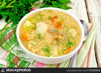 Soup fish kulesh with millet, potatoes and carrots in a white bowl on a napkin, parsley, dill on a light wooden board background