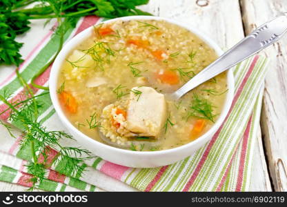 Soup fish kulesh with millet, potatoes, carrots and spoon in a white bowl on a napkin, parsley, dill on a light wooden board background