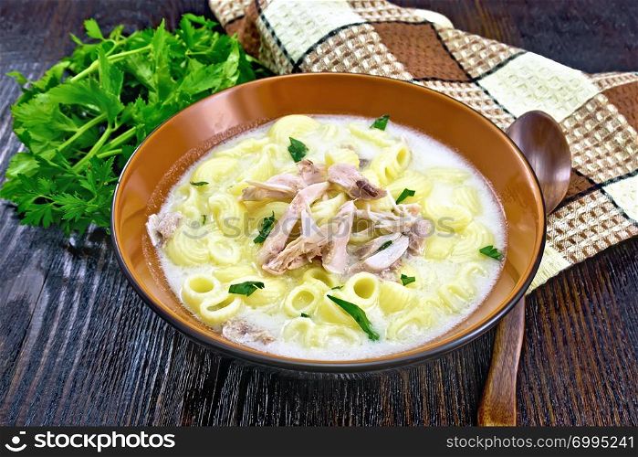 Soup from chicken meat, pasta with cream and cilantro in a clay plate, napkin, parsley, spoon on a wooden board background