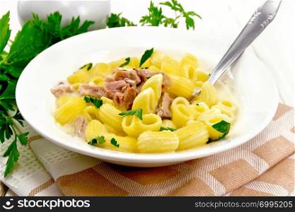 Soup from chicken meat, pasta with cream and cilantro in a plate, towel, parsley, metal spoon on the background of a light wooden board