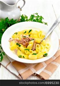 Soup from chicken meat, pasta with cream and cilantro in a plate on a kitchen towel, parsley, metal spoon on a wooden board background
