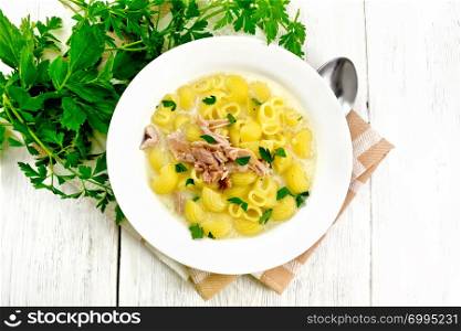 Soup from chicken meat, pasta with cream and cilantro in a plate, napkin, parsley, metal spoon on a wooden board background from above