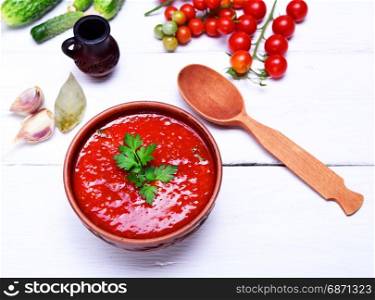 Soup gazpacho in a brown plate on a white wooden background with a wooden spoon, top view