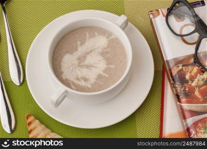 soup in a white bowl with book and glasses on a green tablecloth. soup and a book on a green tablecloth