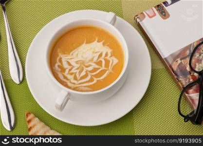 soup in a white bowl with book and glasses on a green tablecloth. soup and a book on a green tablecloth