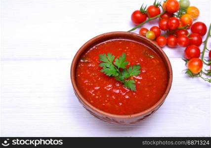 Soup of fresh red tomato gazpacho in a ceramic brown plate on a white table, empty space
