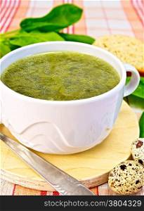 Soup of green nettles, sorrel, spinach, rhubarb leaves on a round wooden board, bread, quail eggs, spoon on a cloth background