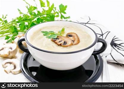 Soup puree from ch&ignons, potatoes, onions and cream in a bowl, napkin, parsley and spoon on a background of white wooden board