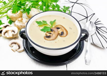 Soup puree from champignons, potatoes, onions and cream in a bowl, a kitchen towel, parsley and a spoon on wooden board background