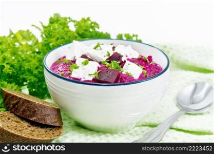 Soup puree of beetroot, potato and cream with salted cream cheese in a bowl on kitchen towel, bread and parsley on a white wooden board background