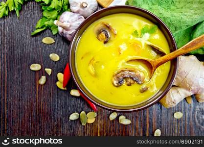Soup-puree pumpkin with prawns and champignons, a spoon in a brown bowl, napkin, parsley, pumpkin seeds, ginger on a wooden board background