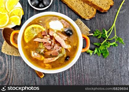 Soup saltwort with lemon, meat, pickles, tomato sauce olives in a bowl on a sacking, bread on a background of a wooden board from above