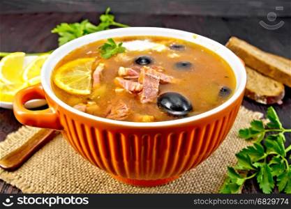 Soup saltwort with lemon, meat, pickles, tomato sauce olives in a bowl on a sacking, bread and parsley on a wooden board background
