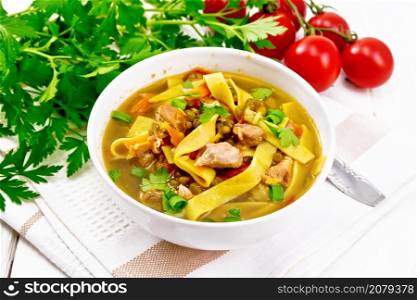 Soup with meat, tomatoes, vegetables, mung bean lentils and noodles in a bowl on napkin, parsley and a spoon on wooden board background