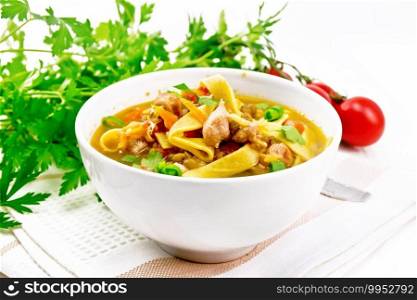 Soup with meat, tomatoes, vegetables, mung bean lentils and noodles in a bowl on a towel, parsley and spoon on the background of light wooden board