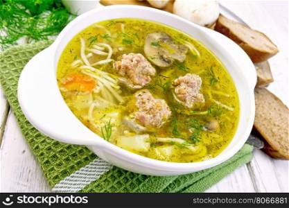 Soup with meatballs, noodles and mushrooms in a white bowl on a green napkin, parsley on a wooden boards background