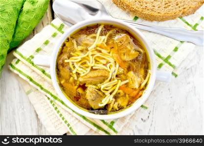 Soup with noodles and mushrooms in a white bowl on a napkin, bread on the background of wooden boards on top