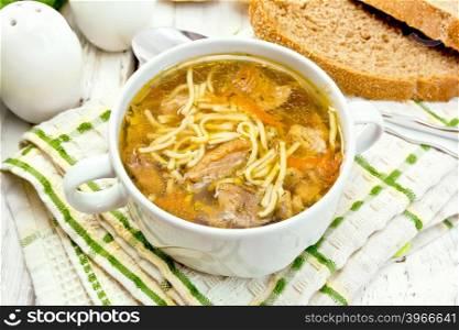 Soup with noodles and mushrooms in a white bowl on a napkin, bread on the background light wooden boards
