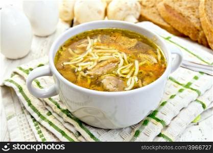 Soup with noodles and mushrooms in a white bowl on a napkin, bread on a wooden boards background