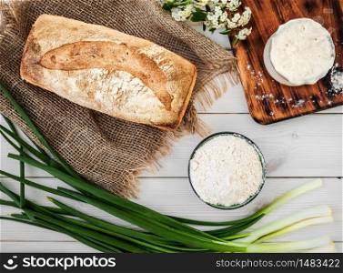 Sourdough for the preparation of bread, flour and freshly baked bread on a white wooden table. Hobbies, baking bread at home. Healthy food concept, traditional craft bread. Layout