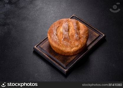 Sourdough rustic homemade hea<hy bread. Traditional bread, home baking. Tasty fresh baked in oven white bread on a dark concrete background