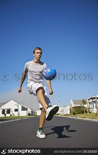 South Africa, Cape Town, teenage boy kicking ball on street