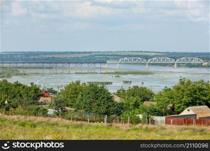 Southern Bug river and rural summer landscape. View of the village, wide river, railway bridge and foggy sky. Copy space.. Rural summer landscape with village views, wide river, railway bridge and foggy sky.