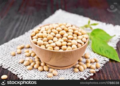 Soy beans in a bowl, green leaf on burlap on wooden board background