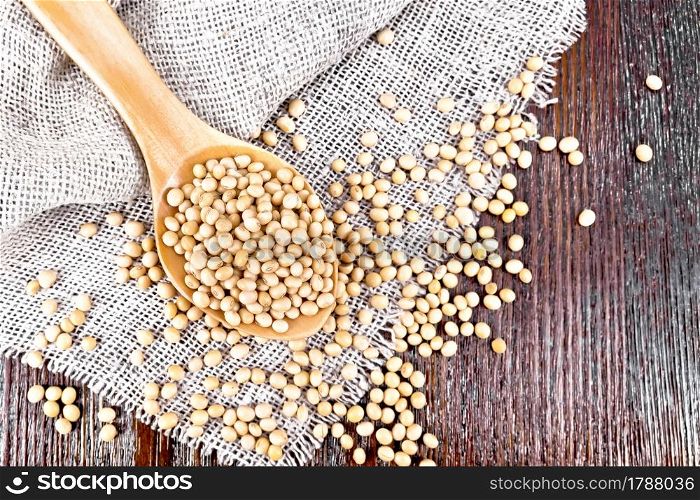 Soy beans in a spoon on sacking on a dark wooden board background from above