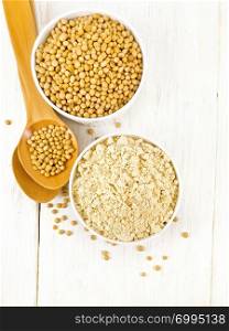 Soy flour and soybeans in two white bowls, spoons on a wooden board background from above