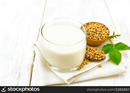 Soy milk in a glass, green leaf, soybeans in a spoon and bowl on a napkin on the background of wooden boards