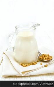 Soy milk in a jug, soybeans in a spoon and on a napkin against a wooden board
