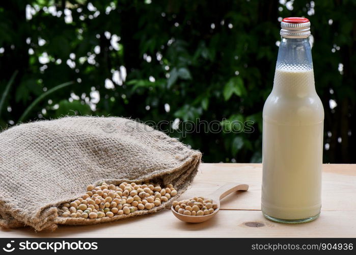 Soy milk in bottles and soy on a spoon Poured out from the hemp sack bag on the wooden floor