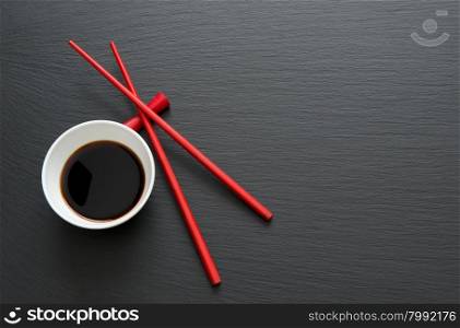 Soy sauce with red chopsticks on black slate table