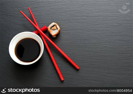 Soy sauce with red chopsticks on slate background